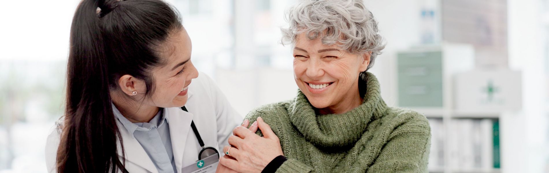 Happy, care and face of a doctor with a woman for medical trust, healthcare and help. Laughing, hug and portrait of a young nurse with a senior patient and love during a consultation at a clinic caring orthopedic doctor